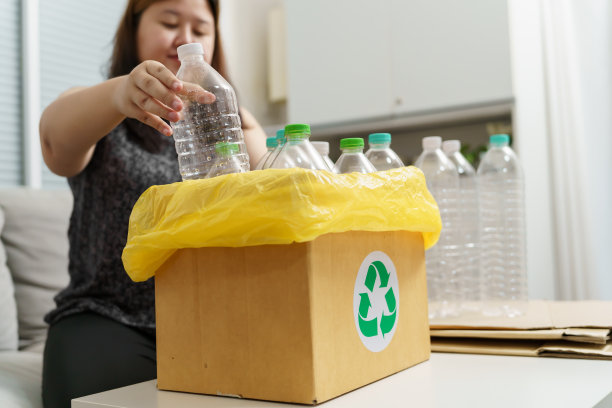 家庭回收生态绿色零概念妇女将空塑料瓶扔进装有黄色垃圾袋的回收箱。图片下载