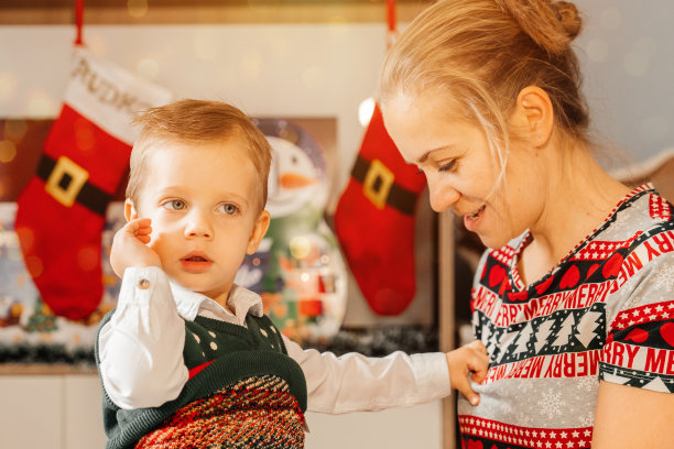 可爱的年轻母亲带着儿子靠近圣诞树，新年和圣诞节的概念。圣诞图片，树和灯的背景。圣诞快乐，新年快乐。年轻快乐的母亲和她可爱的小儿子正在庆祝圣诞节或新年。图片下载
