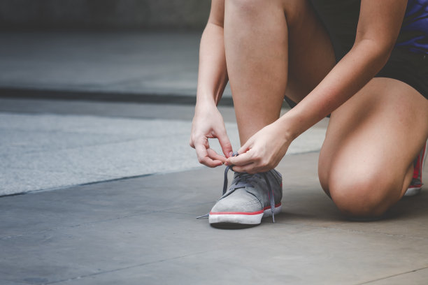 年轻女子跪下来系鞋带。在运动锻炼中准备跑鞋慢跑者。近距离的手绑跑步者的鞋带在健身房健康的人的生活方式。图片下载