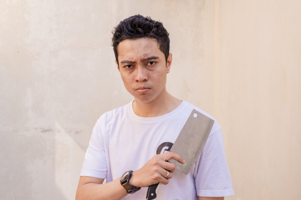 印尼男人准备摆姿势的时候，手里拿着屠刀，穿着白色的t恤。图片下载