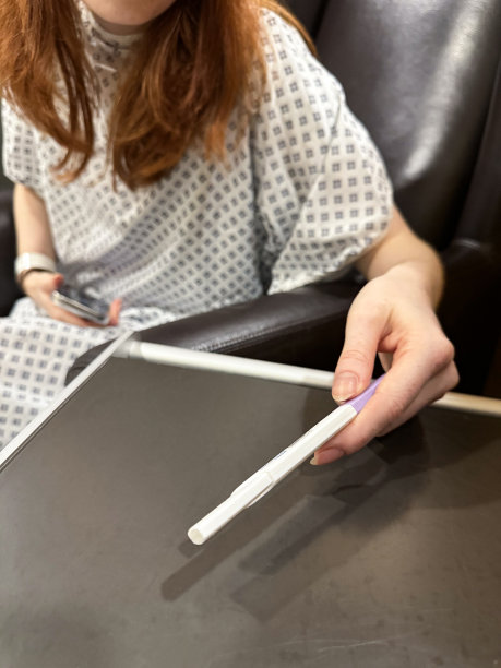 特写照片中，无法辨认的红发女人穿着医院的长袍，坐在医院候诊室的皮革扶手椅上，看着怀孕测试，鼻中隔成形术(鼻中隔偏曲手术和鼻子整形)，重点放在前景图片下载