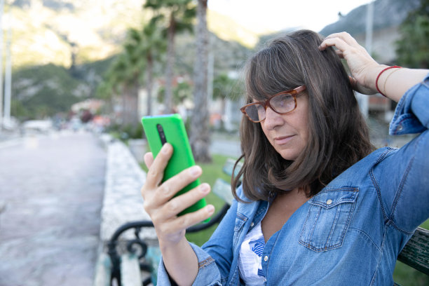 坐在海边长凳上的白发老人微笑着看着他的智能手机。迷人的人们微笑着享受户外和大自然的美丽。老年人和现代科技股票照片…图片下载