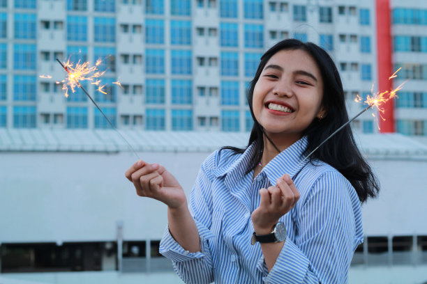 快乐的亚洲年轻女商人手持烟花，站在以城市建筑为背景的户外屋顶上庆祝新年图片下载