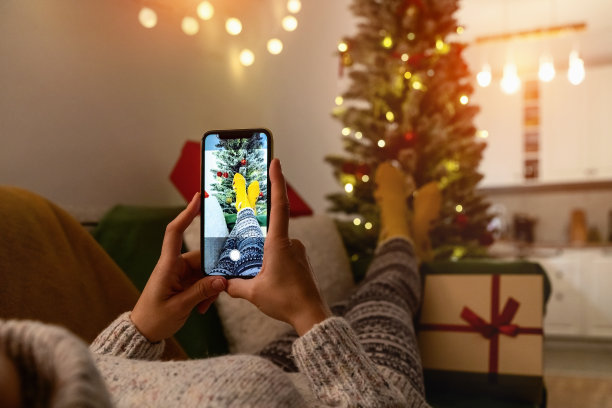 一个女人躺在沙发上，在圣诞树前拍她穿着袜子的脚的照片。圣诞节期间的照片短信。图片下载