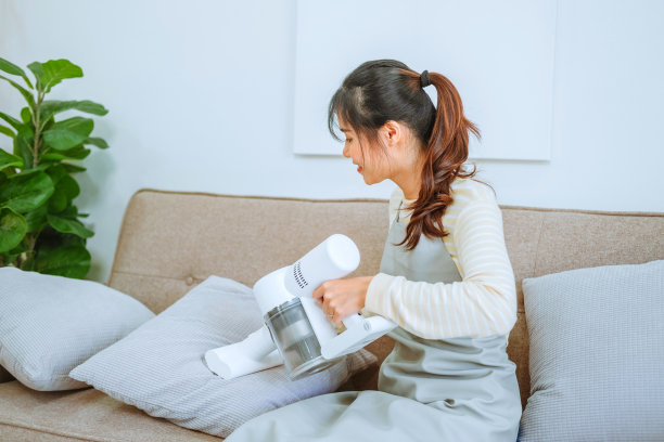 亚洲妇女用吸尘器清洁沙发。管理的概念图片下载