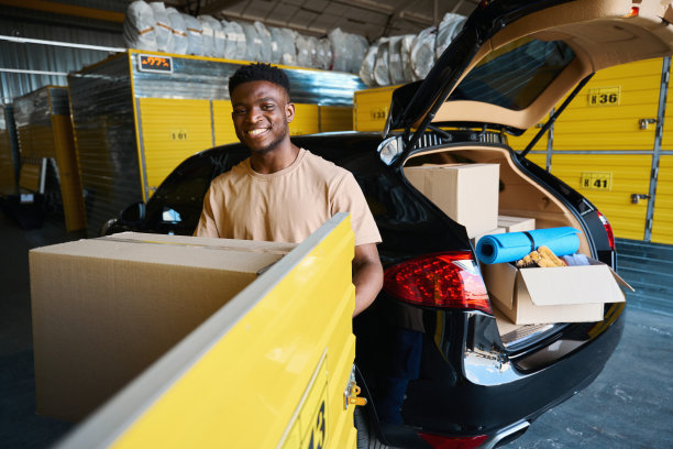 一个面带微笑的男人把一个装着东西的纸板箱装进黄色牢房图片下载
