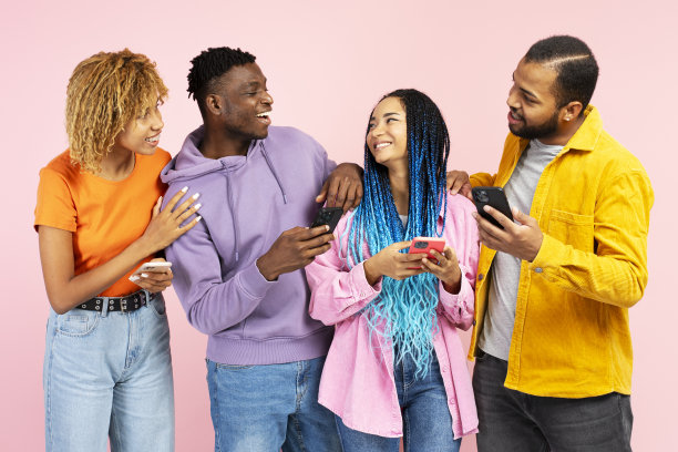 迷人的微笑的非裔美国朋友拿着手机，交流，交谈孤立在粉红色的背景。科技，友谊理念图片下载
