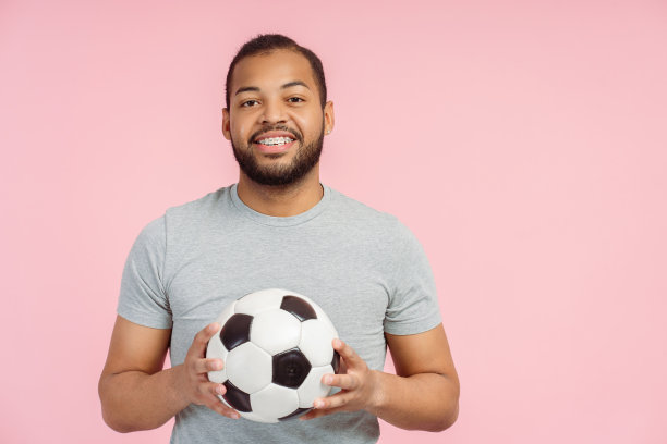 迷人的微笑的非洲裔美国人的肖像拿着足球孤立在粉红色的背景图片下载