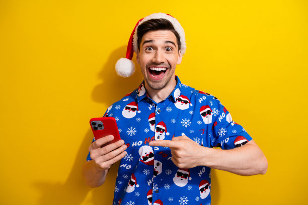 疯狂交易的照片新年假期指着全新的智能手机圣诞老人帽子孤立的黄色背景图片下载