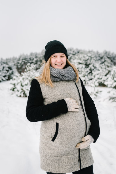 年轻的孕妇穿着暖和的衣服，在美丽的冬日雪天玩耍。在冬天的山区度假胜地度过孕期。女性在公园或森林散步。冬天的假期。图片下载