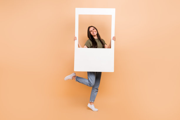 全长照片的酷兴奋的女孩穿着卡其布t恤上升纸相框孤立米色背景图片下载