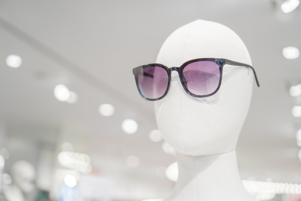 一个秃顶的白色人体模特戴着紫色的太阳镜。一家服装商店在购物中心的展示。图片下载