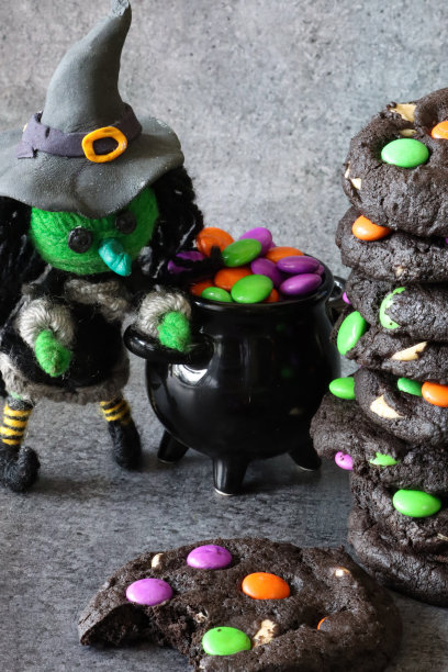 一堆新鲜出炉的自制万圣节的特写图片，白色的巧克力片，黑色的可可饼干装饰着粉红色，绿色和橙色的糖果涂层巧克力糖果，绿色的羊毛女巫，黑色的大锅，饼干缺失的咬，重点在前景图片下载