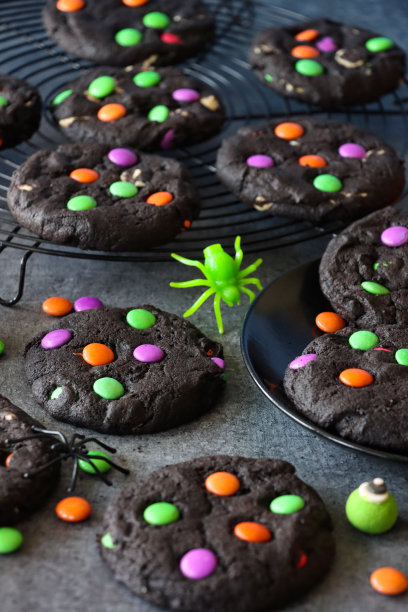 自制万圣节的特写图片，白色巧克力片，黑色可可饼干放在冷却架和盘子上，用粉红色、绿色和橙色的糖果装饰巧克力糖果，塑料蜘蛛，防油纸羊皮纸背景，重点在前景图片下载