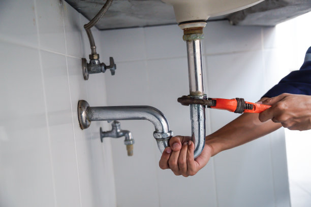 在浴室工作的水管工，管道维修服务，用活动扳手修理漏水的水槽，组装和安装概念。图片下载