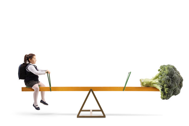 一个女学生的全身侧面照片和西兰花蔬菜在跷跷板上，健康饮食的概念图片下载