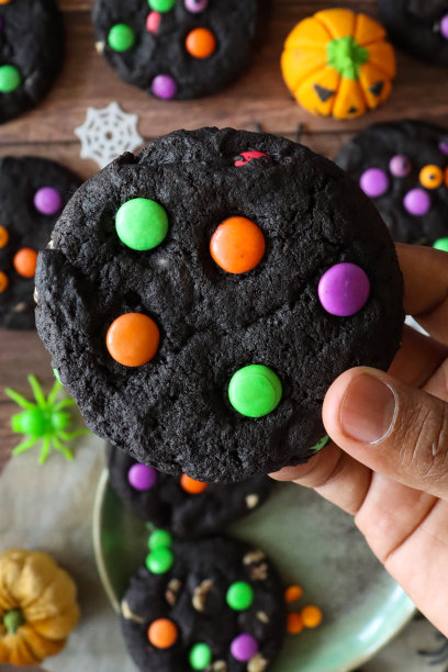 特写图片无法辨认的人拿着自制的万圣节，白色巧克力片，盘子上的黑可可饼干，装饰着粉红色，绿色和橙色的糖果涂层的巧克力糖果，塑料蜘蛛，蜘蛛网，毛绒南瓜，高架视图图片下载