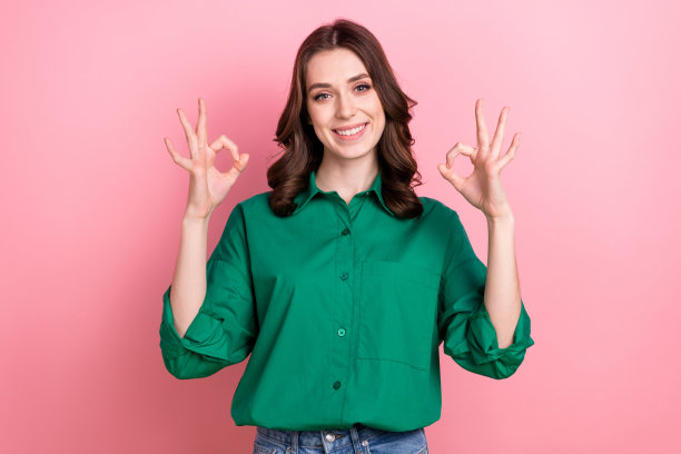 照片中，自信闪亮的女人穿着绿色衬衫，在粉红色的背景下展示了两个不错的手势图片下载