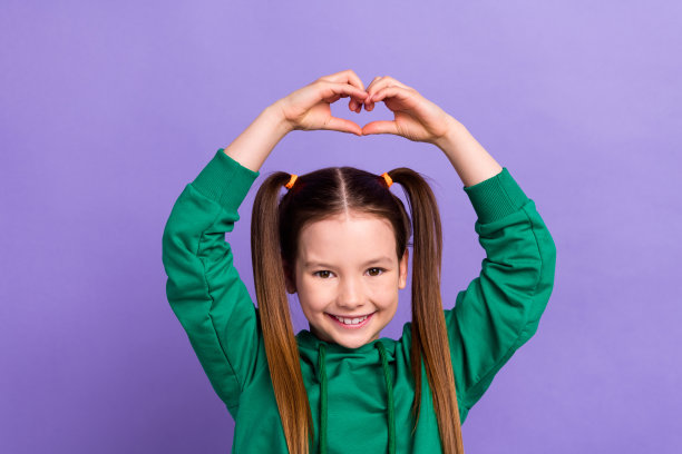 照片开朗可爱的女孩棕色的头发尾巴显示心的姿态同情爱人享受幼儿园孤立的紫罗兰色背景图片下载
