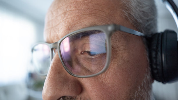 老人戴着眼镜和无线耳机看书图片下载