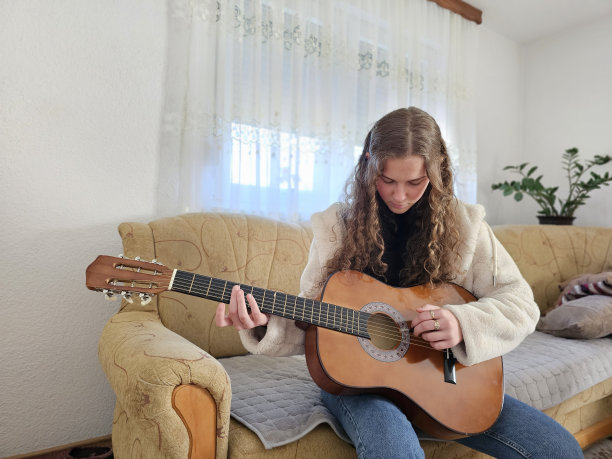 这位年轻的卷发女孩在舒适的家中充满激情和天赋地弹奏着原声吉他，在这张现实主义的照片中创造出美丽的旋律图片下载