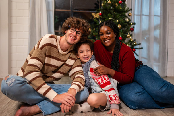 多民族家庭在家里庆祝圣诞晚会的照片。有魅力的年轻父母和他们的小女儿坐在一起享受圣诞节、感恩节的节日，看着镜头。图片下载