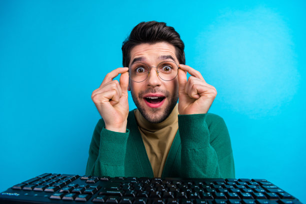 兴奋的年轻人程序员靠近机械键盘的特写照片，数字技术极客惊讶地孤立在蓝色背景上图片下载