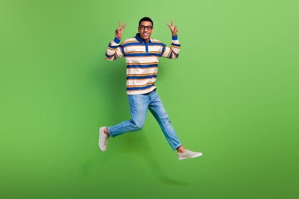 青年男硕士学生的全身照片终于完成了他的教育显示v标志胜利标志跳跃孤立的绿色背景图片下载