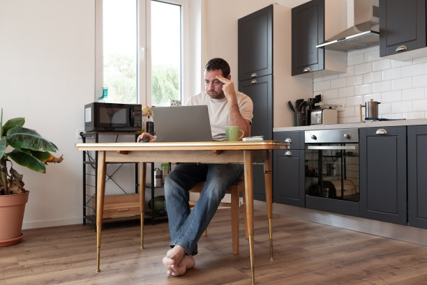 有压力的人在厨房用笔记本电脑工作。图片下载