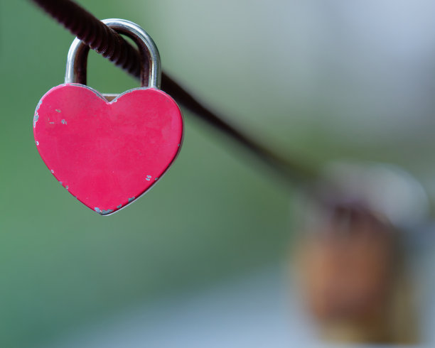 一张粉红色心形挂锁挂在金属丝上的选择性对焦照片，背景模糊图片下载