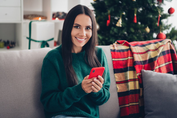 照片正面漂亮可爱的女士坐在沙发上使用电话选择礼物礼物有空闲时间享受休息奇迹的房子房间室内图片下载