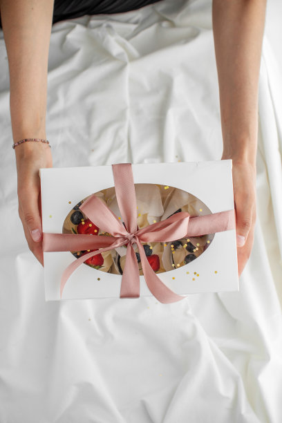 年轻的糕点师拿着一个礼盒，礼盒上有浅色背景的缎带图片下载