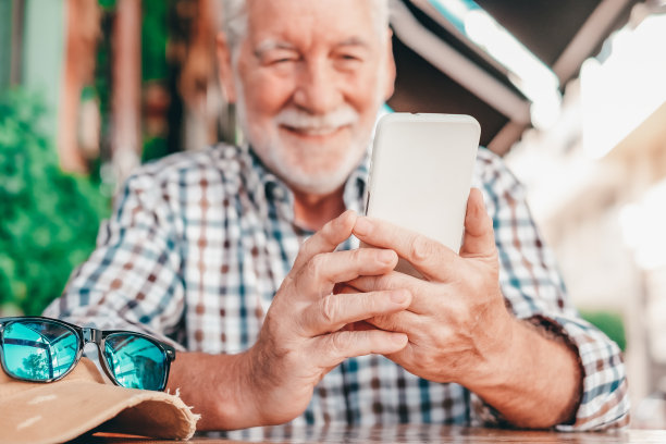 心不在焉的老人拿着手机，坐在户外的咖啡桌旁享受科技和社交，放松的退休生活方式图片下载