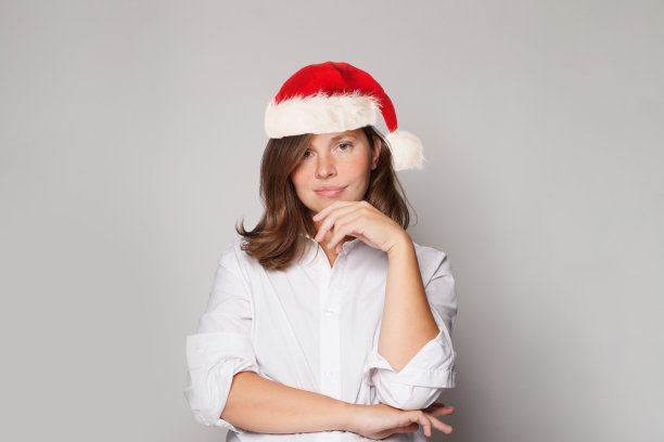 快乐的圣诞妇女戴着圣诞老人的帽子站在白色的背景图片下载