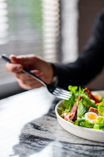 手拿叉子的男人吃沙拉尼斯。金枪鱼，配青豆，西红柿，土豆和白盘子里的油醋酱芥末酱图片下载