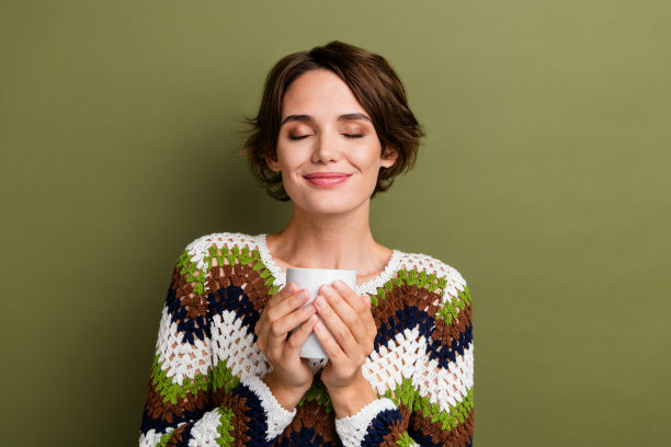 照片的闪亮梦幻的女孩穿着条纹衣服，闭上眼睛享受热可口的可可香气孤立的绿色背景图片下载