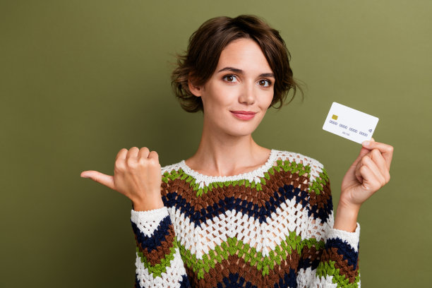 照片中开朗漂亮的女孩穿着条纹衣服，手拿信用银行大拇指，空白空间孤立绿色背景图片下载