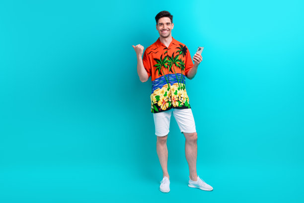 穿着印花衬衫的智能男子的全身照片，手持智能手机，指向蓝色背景上孤立的促销空白空间图片下载