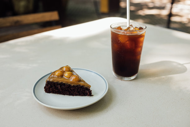 早上，白色的桌子上放着焦糖夏威夷蛋糕和冰黑咖啡。库存图片图片下载
