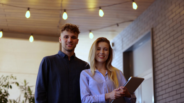 一对快乐的白人夫妇的肖像，一男一女手持笔记本电脑，站在餐厅的室内，看着镜头。积极的年轻男女一起摆姿势，微笑着图片下载