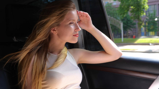 在城市里，一辆汽车后座上坐着一个漂亮的白人金发女郎。肖像。快乐的美女在汽车里看着街道上的窗户。慢动作图片下载