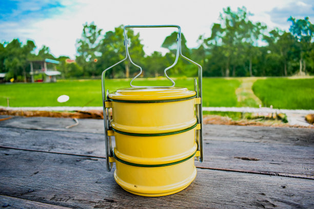 在照片中，一个亮黄色的食品容器矗立在一片广阔、郁郁葱葱的稻田的背景下，给人一种与自然联系在一起的感觉。图片下载