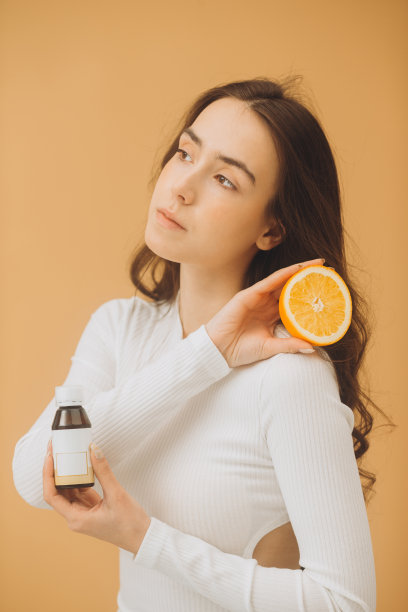 穿橘色衣服的美女。照片的美丽的女人与完美的化妆在裸色背景。美容护肤维生素C概念。图片下载