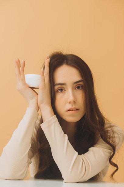 美女拿着一罐保湿霜。米色背景上完美皮肤的女性照片。美容护肤理念。图片下载