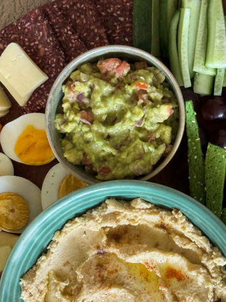 木制的、聚会自助餐的全画幅图片，上面有一碗碗的鳄梨酱和土豆泥，周围是半熟的煮鸡蛋、切达干酪、红葡萄、黄瓜和饼干图片下载