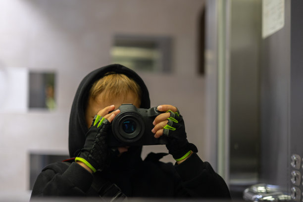 这个男孩在电梯里对着镜子照了一张自己的照片。一个孩子拿着相机拍下了他在电梯镜子里的倒影。一个小孩在电梯里对着镜子自拍。图片下载