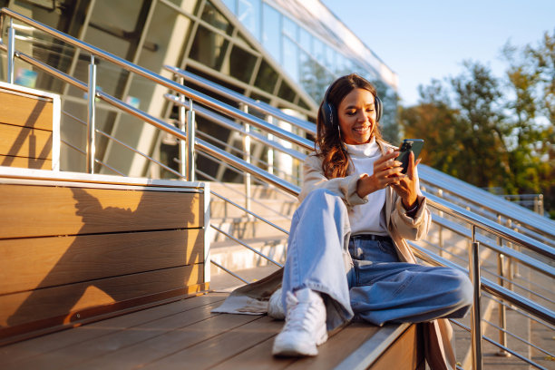 微笑的女人穿着时髦的衣服，拿着电话和无线耳机听音乐。图片下载