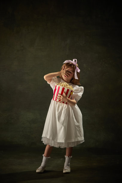 在复古的背景下，受惊的女孩带着一桶爆米花的肖像。电影里的童话故事里的仙女公主的角色在手臂上瞥了一眼。图片下载