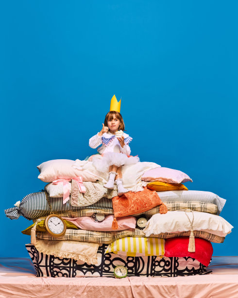 小公主戴着黄色皇冠，坐在一大堆枕头上，拇指向上翘起甜甜的、可口的、美味的蛋糕。图片下载