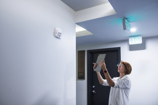 理赔代理人拍摄安装火灾报警器的照片并寄给保险公司。女理赔员报告火灾报警系统。戴眼镜的红头发理赔代理人检查入口处附近的火警。图片下载